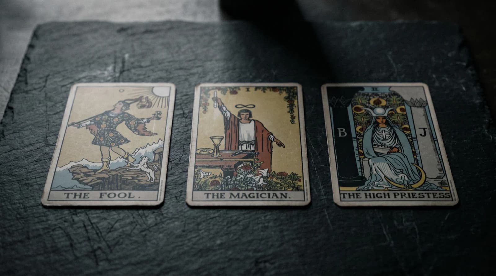 Three tarot cards face-up on warm cream linen, side-lit, near-monochrome editorial photograph